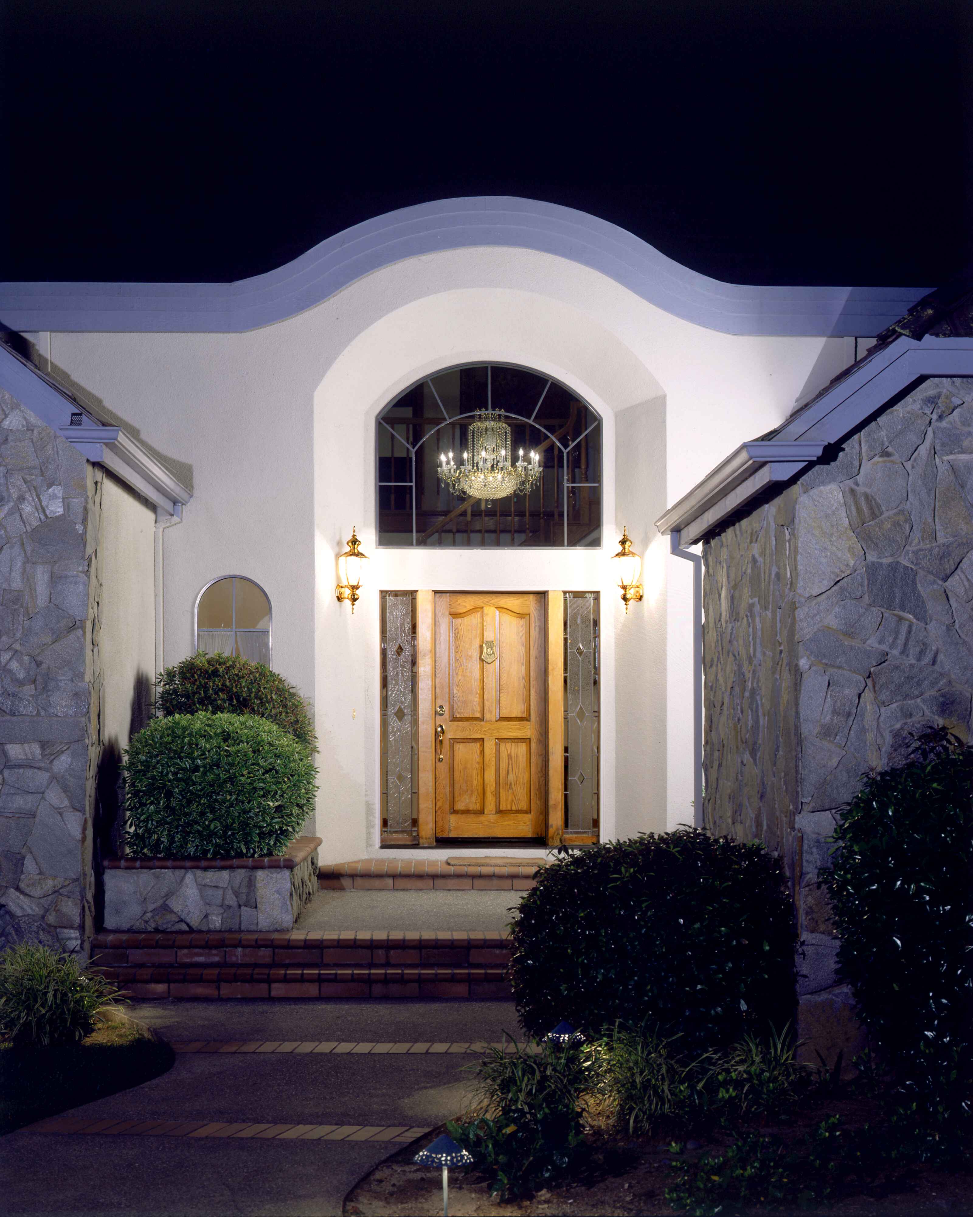Illuminated arched stucco entry with a wood front door on a Sacramento-area home