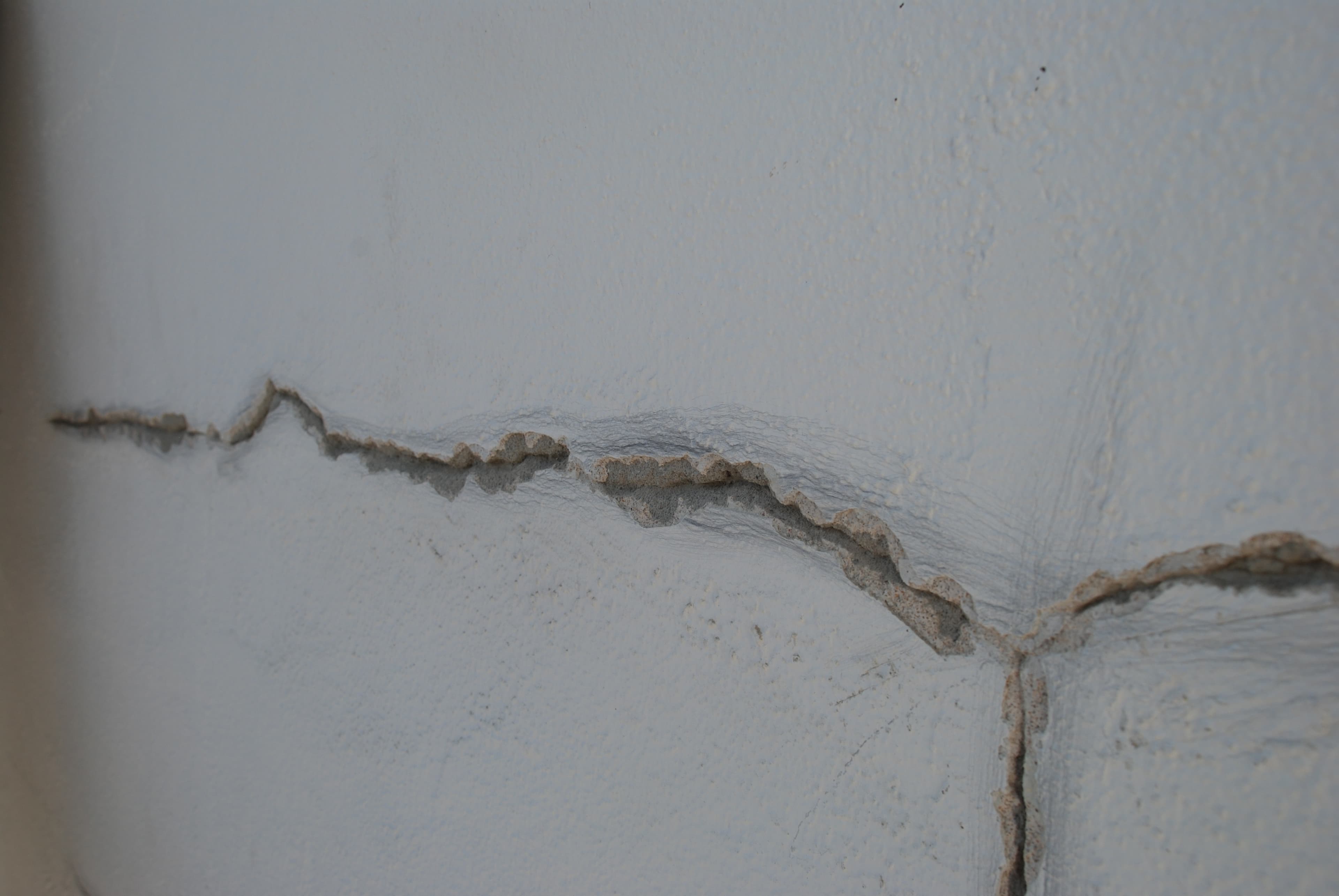 A stucco crack carefully scraped open to remove loose material before repair