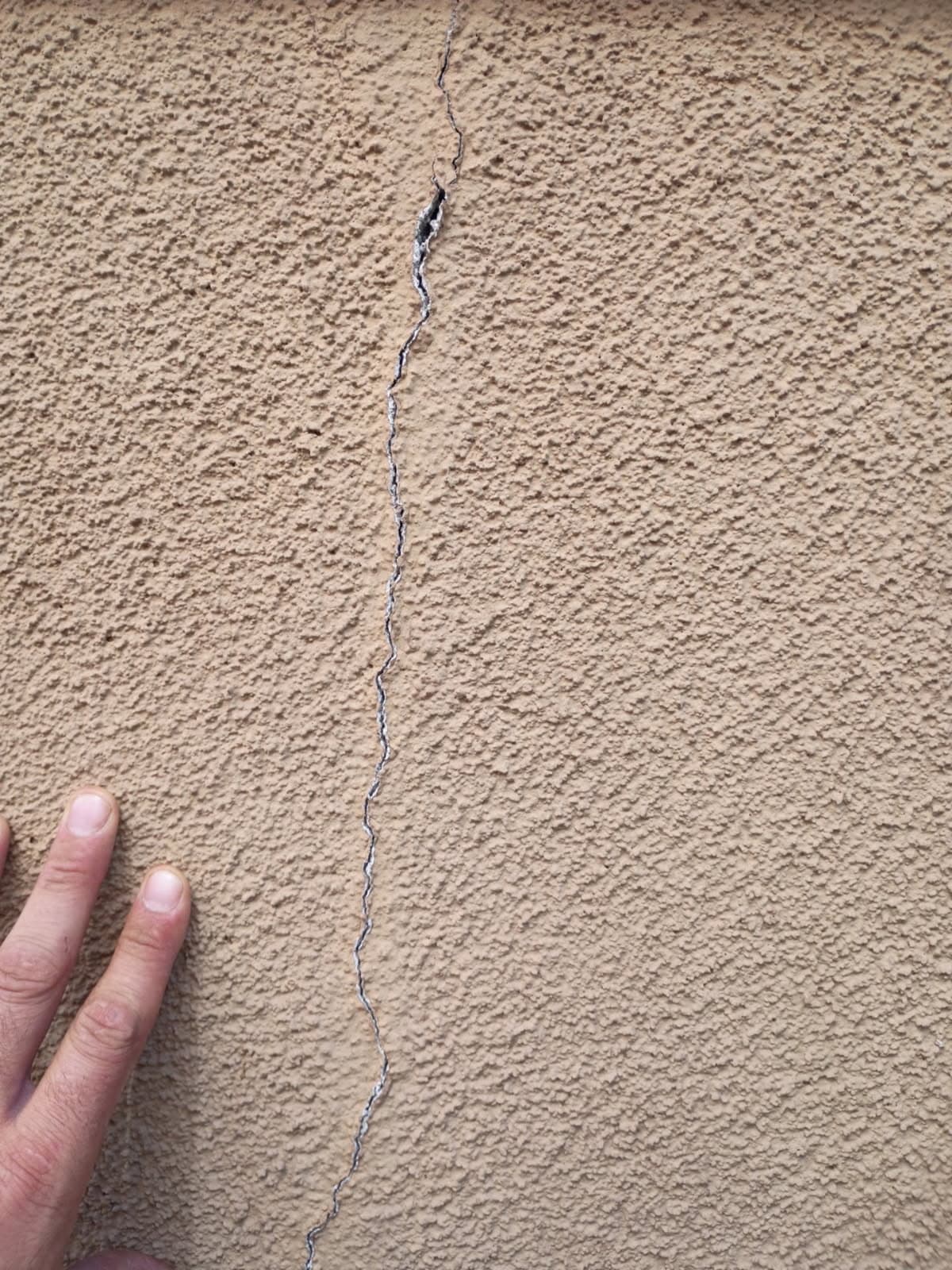 A long vertical crack running down a tan stucco wall on a Sacramento area home, with a hand beside it for scale