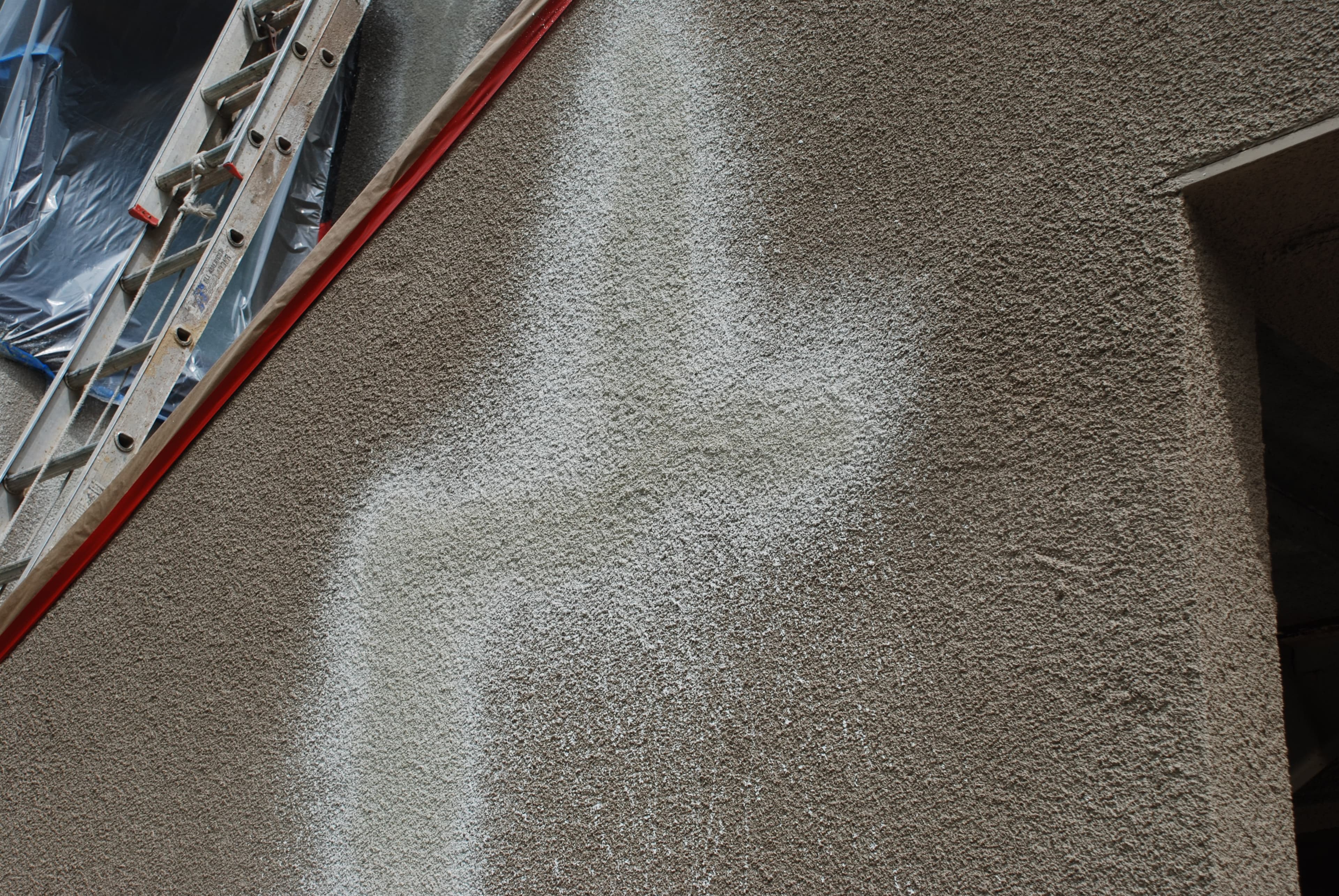A repaired stucco wall with a sprayed texture coat being blended into the existing exterior finish