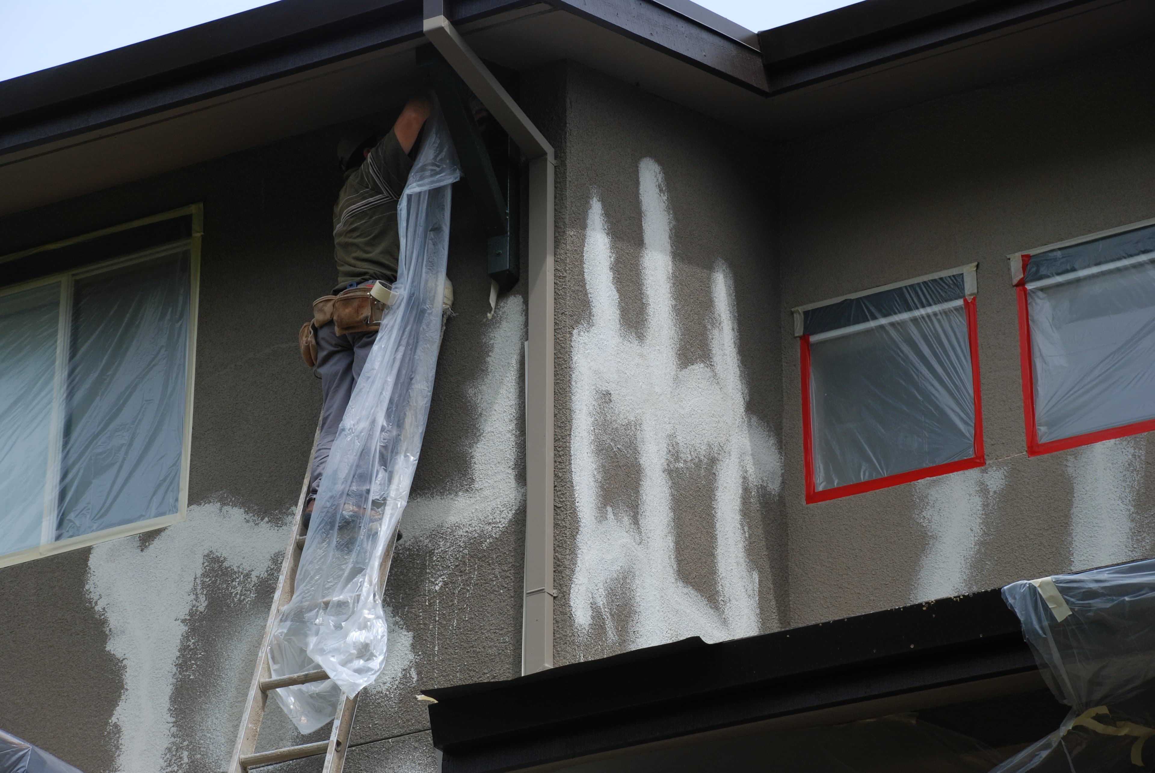 A HomePRO crew member working on a stucco exterior near window openings
